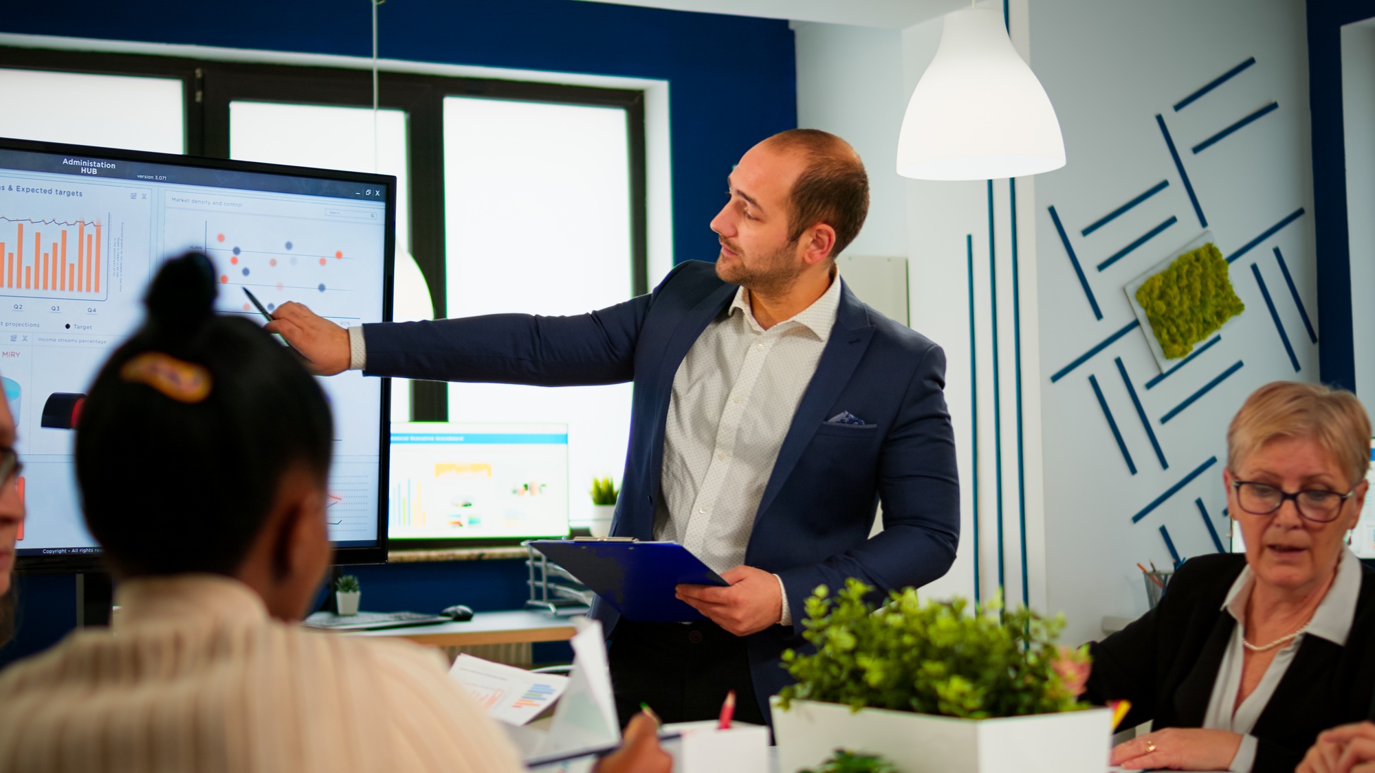 Comapany CEO holding clipboard and pointing on digital interactive whiteboard