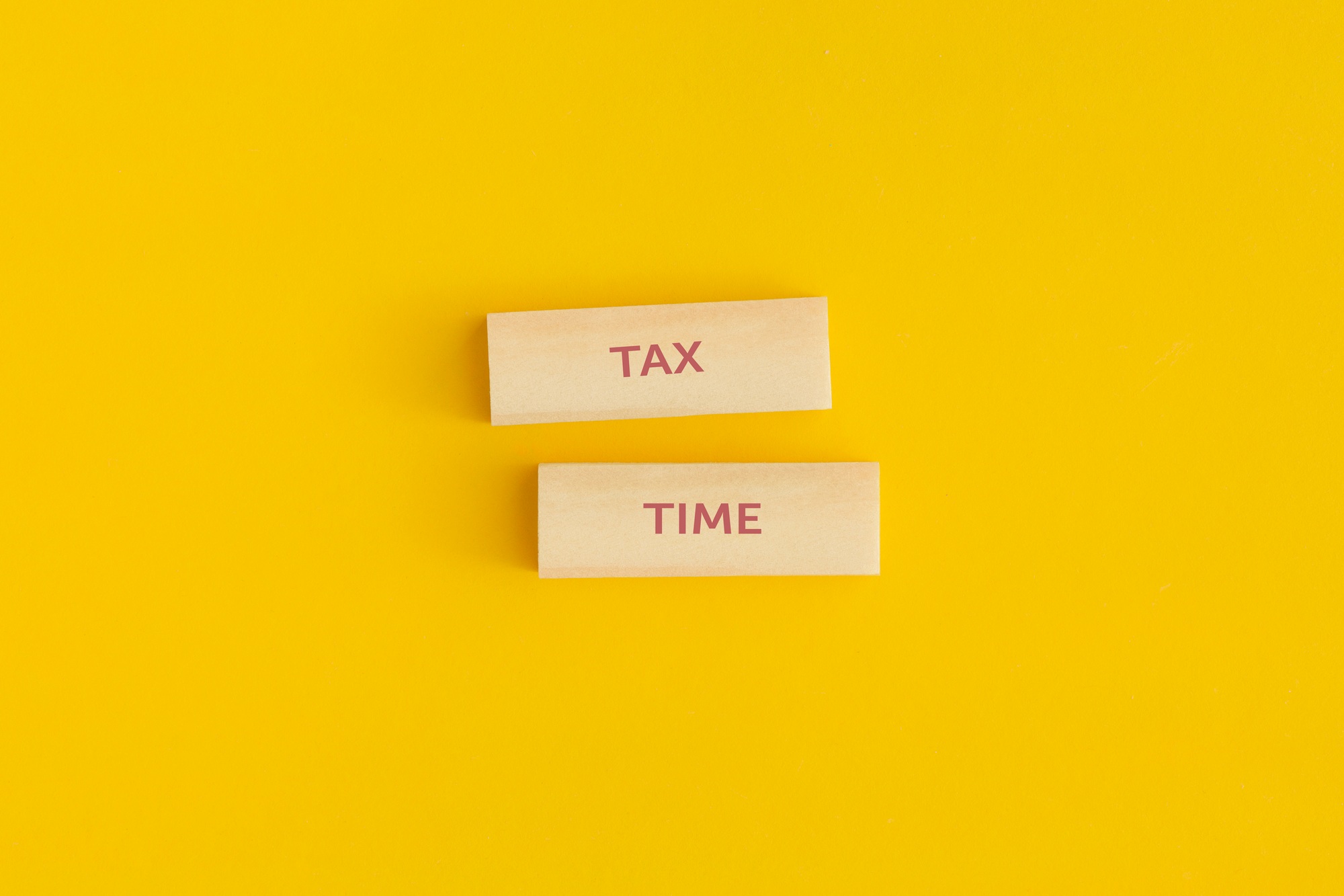 The text "Tax time" on wooden blocks on yellow background.