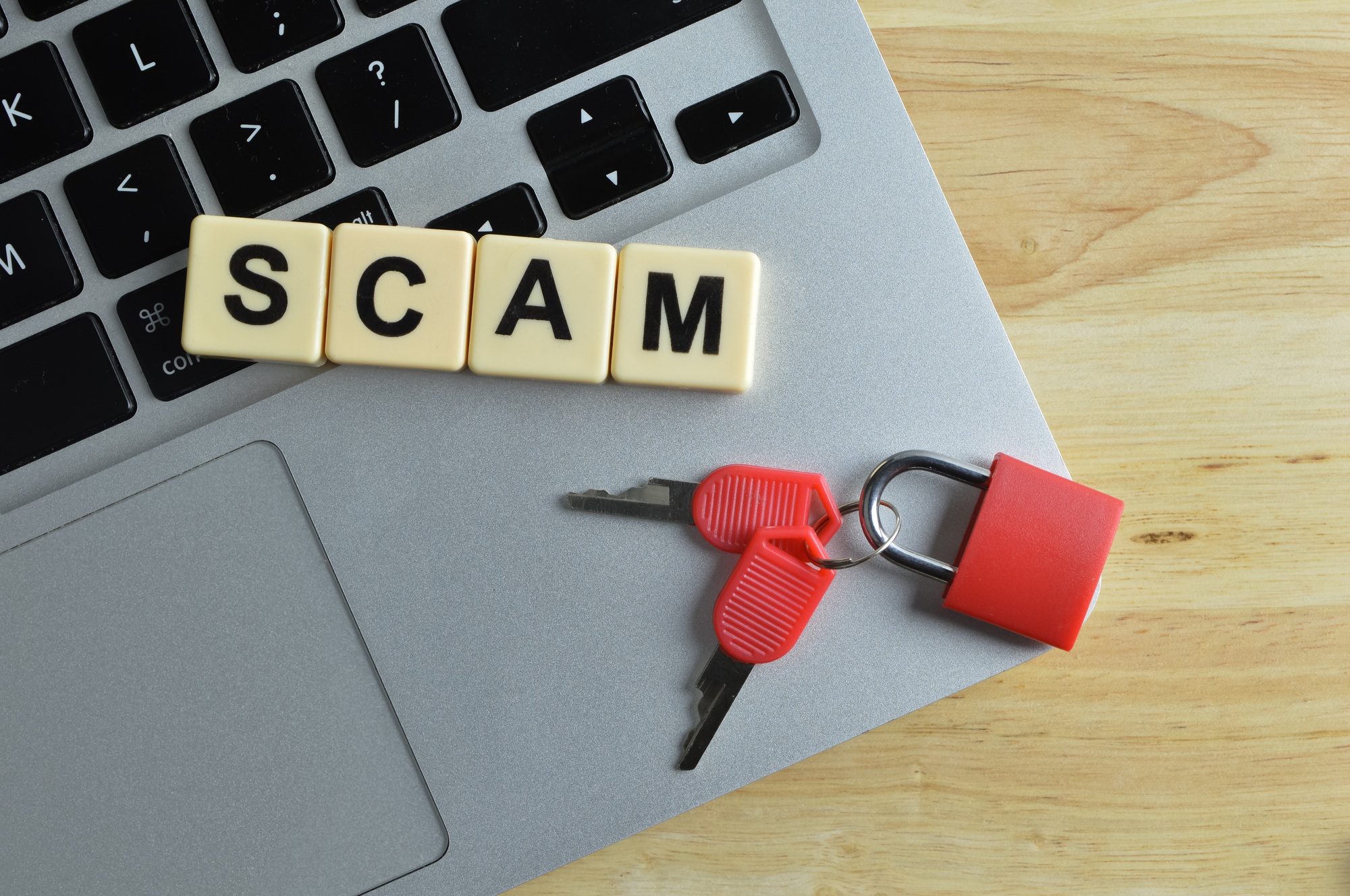 Top view of laptop, toy padlock, keys and scrabble letters with text SCAM.